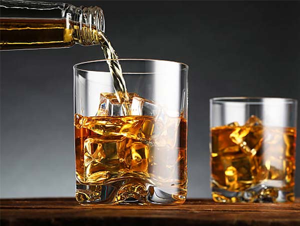 Vaso con whisky servido sobre hielo, con una botella vertiendo la bebida.