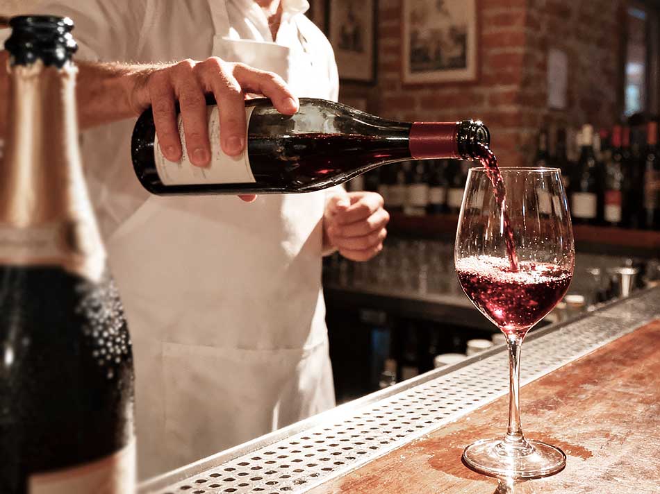 Camarero sirviendo vino tinto, posiblemente sin alcohol, en una copa.